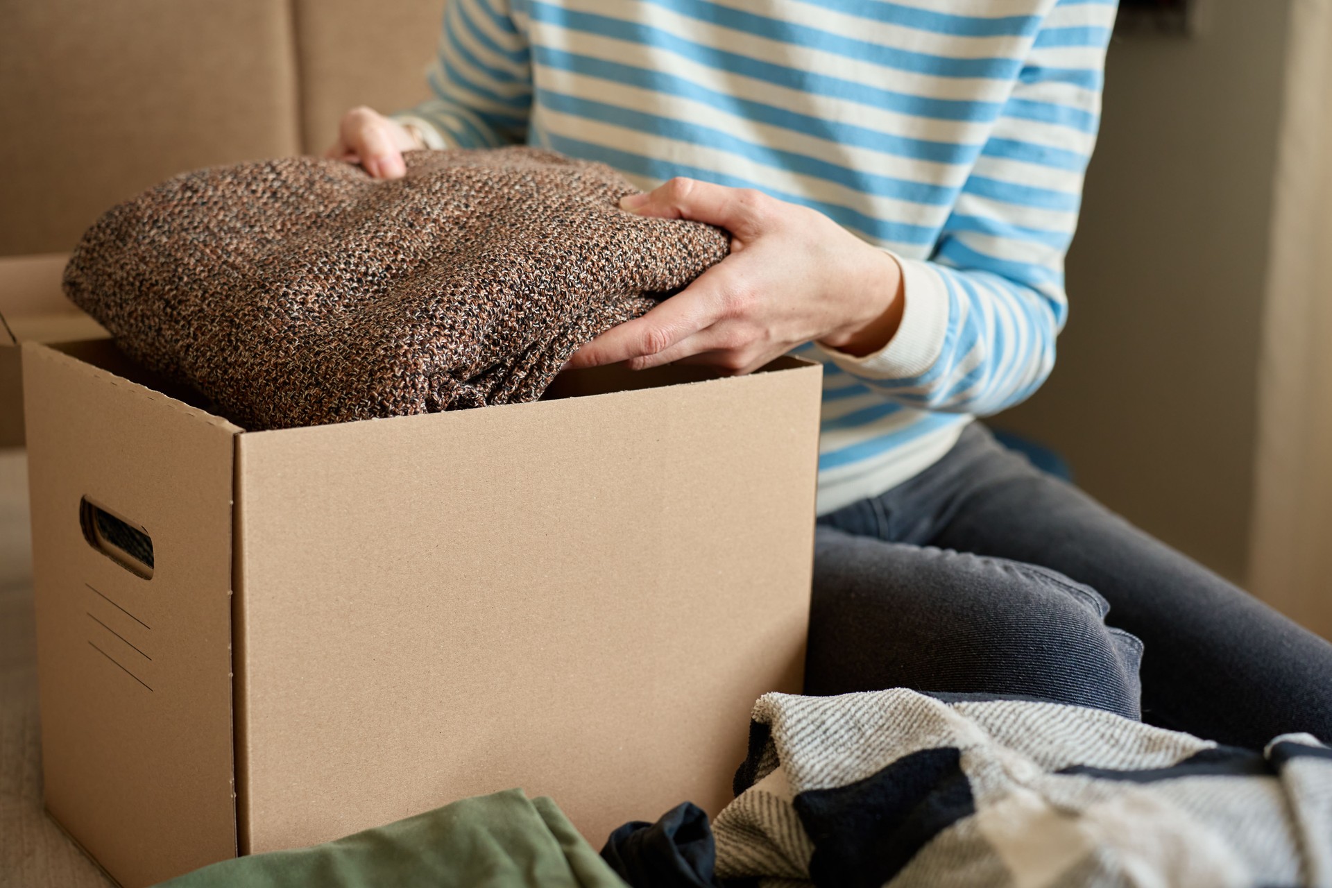 Woman packing donation box, preparing used clothes for charity